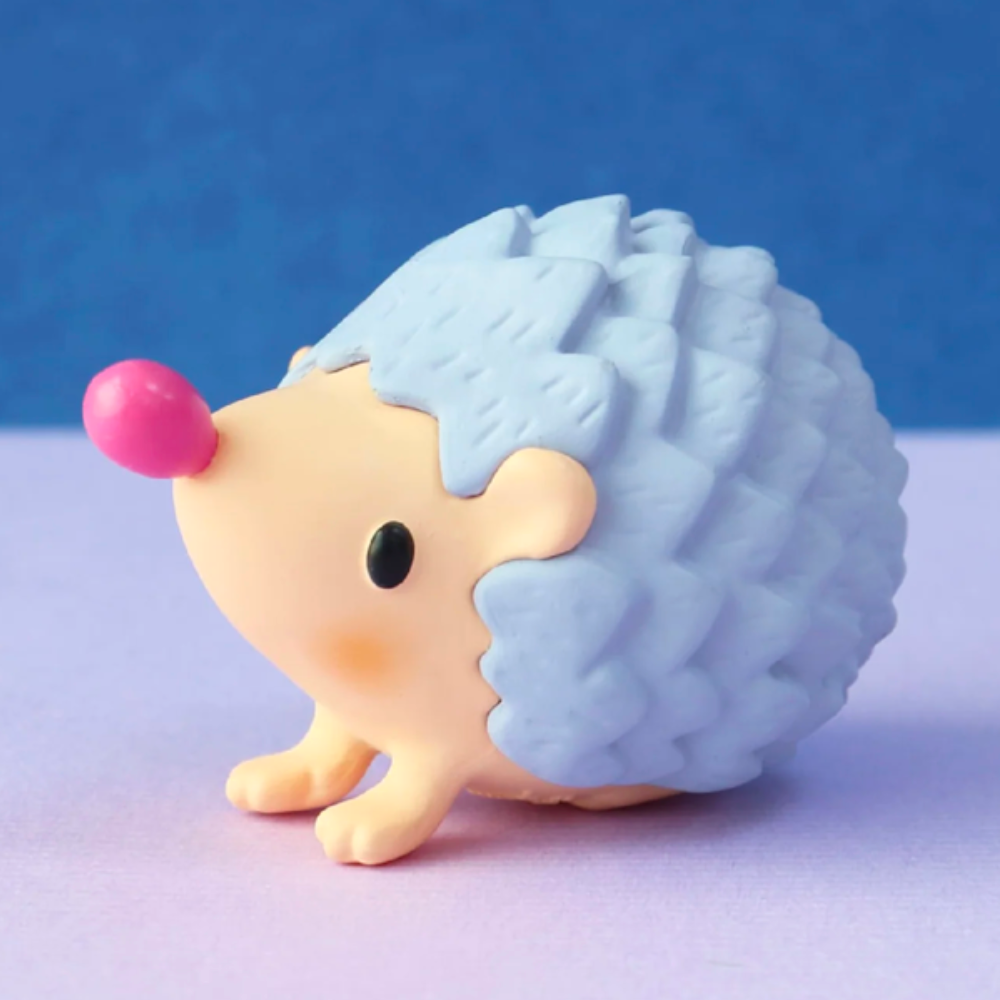 A charming little hedgehog figurine, exuding pure-heartedness, features blue spikes and a pink nose and is perched on a two-toned blue and purple platform, as if unveiled from the enchanting 