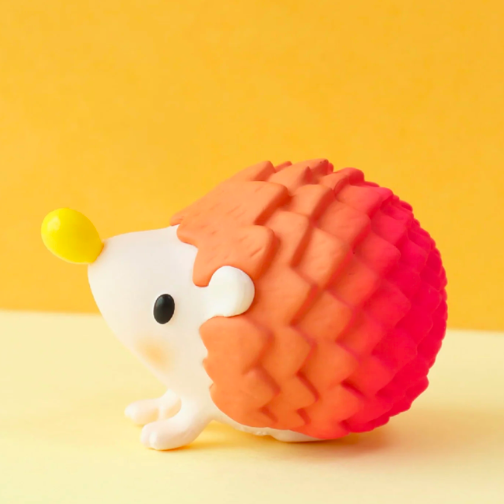 A delightful toy hedgehog from the Good Hedgehog/Bad Hedgehog Blind Box by Partner Toys, featuring a red and orange textured body with a yellow nose, sits against a vibrant yellow background, waiting to be discovered.