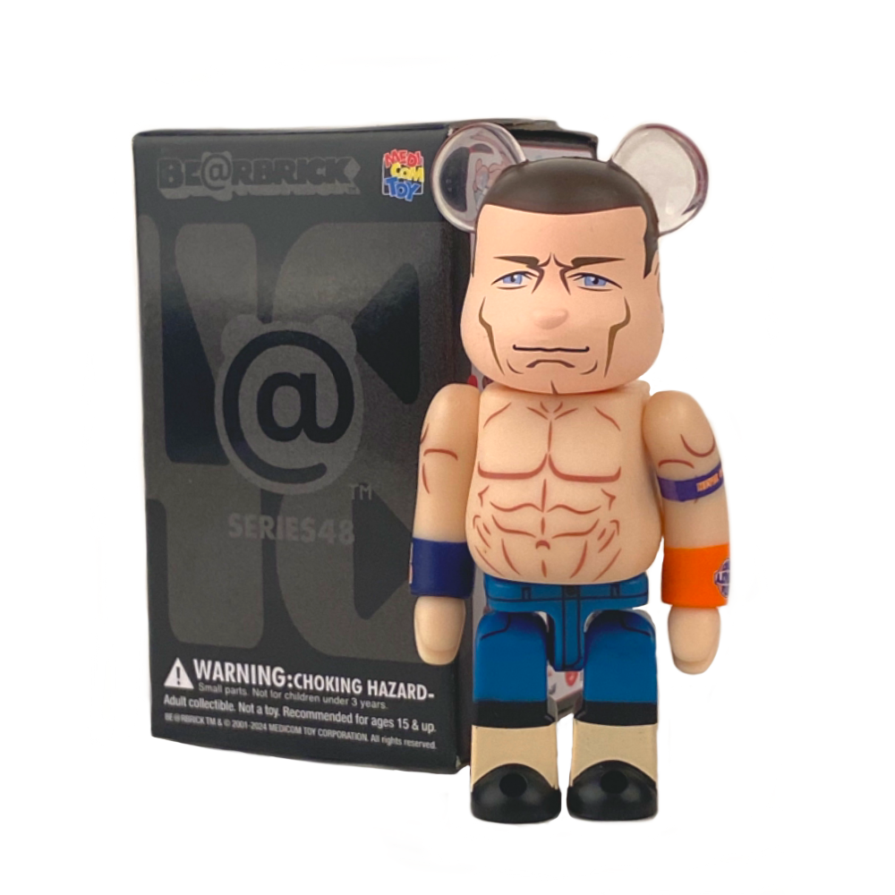 A Be@rbrick toy figure resembling a muscular character with arm bands and blue shorts stands in front of its Medicom (JP) Be@rbrick Series 48 Blind Box.