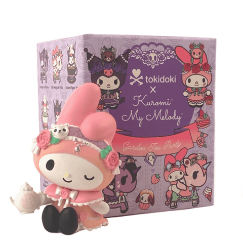 A small My Melody figurine, dressed in pink with a teapot, sits in front of a purple tokidoki x Kuromi & My Melody Garden Party Blind Box featuring Tokidoki characters in costume, bringing the joyous vibe of the garden to life.
