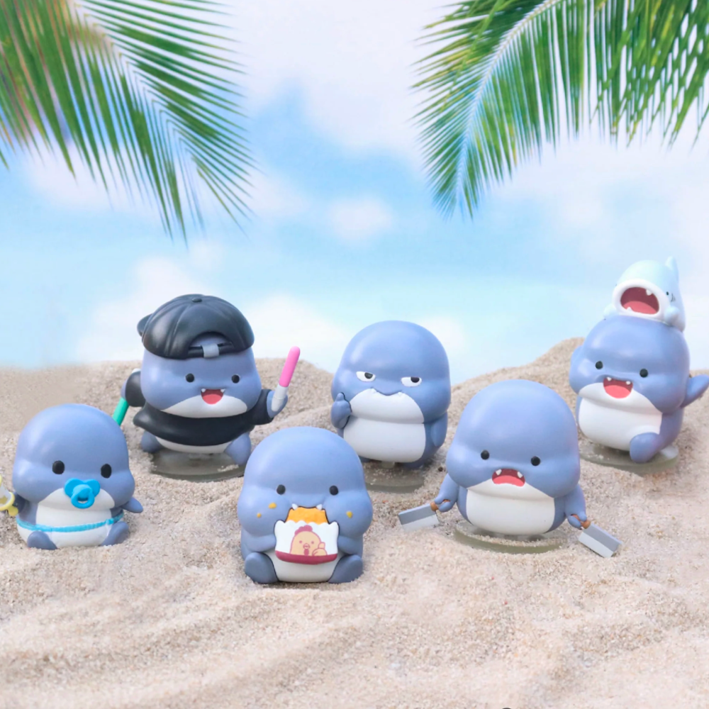 Six cartoonish shark figurines with various accessories are on a sandy beach. Palm leaves can be seen above, and a blue sky with clouds serves as the backdrop, capturing the whimsical essence of a Shahimi Shark — Series 2 Blind Box collection by Partner Toys.