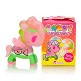 A small figurine of a pink unicorn with green accents and a watermelon-themed body stands next to a colorful box labeled 