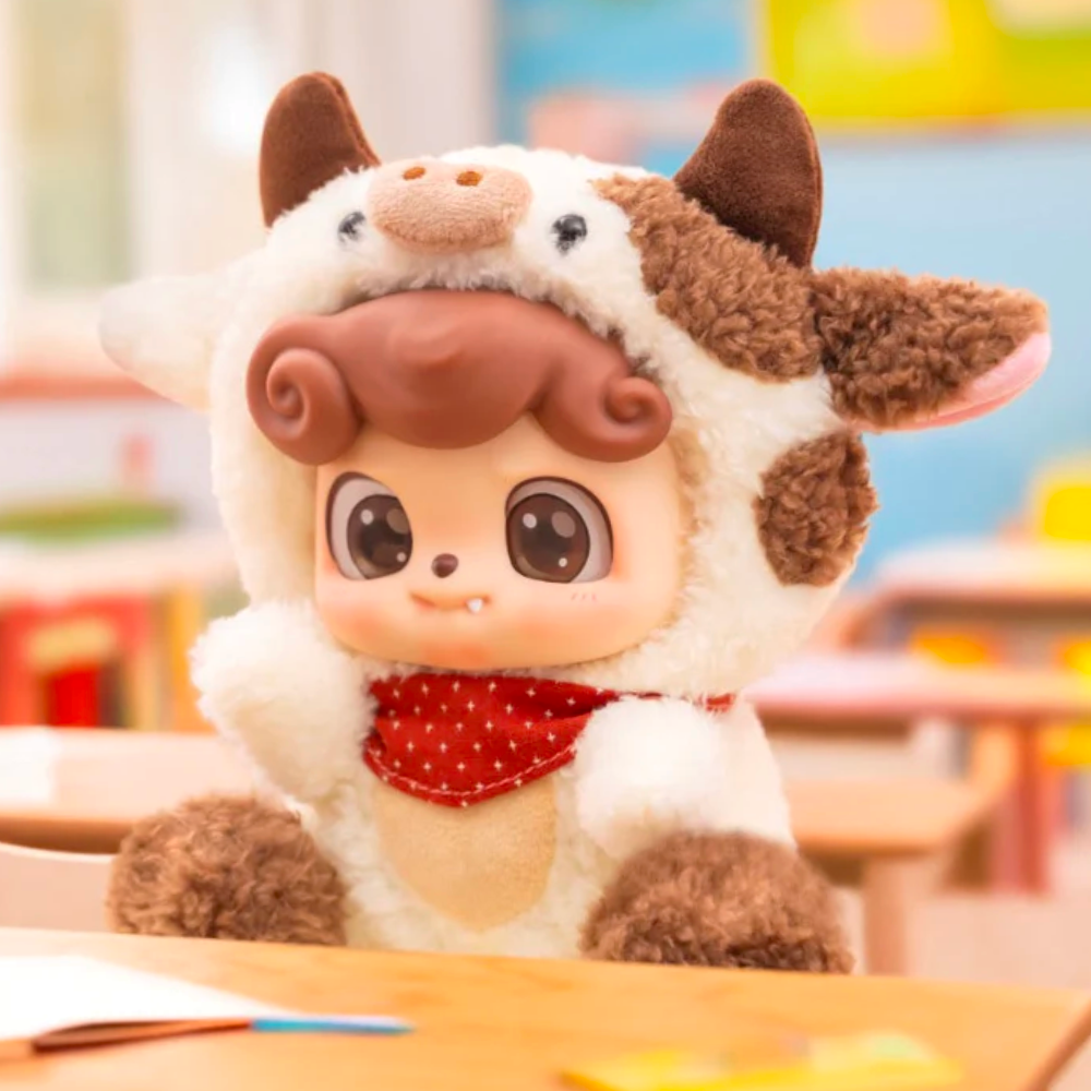 The Q.Kid Animal PreSchool Plush Blind Box by Jotoys, featuring a cute doll face in an animal costume, sits on a desk in the colorful classroom, adding charm to the lively scene.