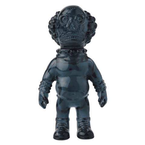 A dark-colored plastic figurine with a large head, exaggerated facial features, and detailed molding standing upright against a white background; it closely resembles the VAG 36 - Deadman by Medicom (JP).