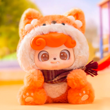 The Jotoys Q.Kid Animal PreSchool Plush Blind Box features a toy figure in a curly orange-haired, fluffy fox costume with ears and a scarf, set against a blurred green and purple background—an adorable keychain addition for animal costume fans.