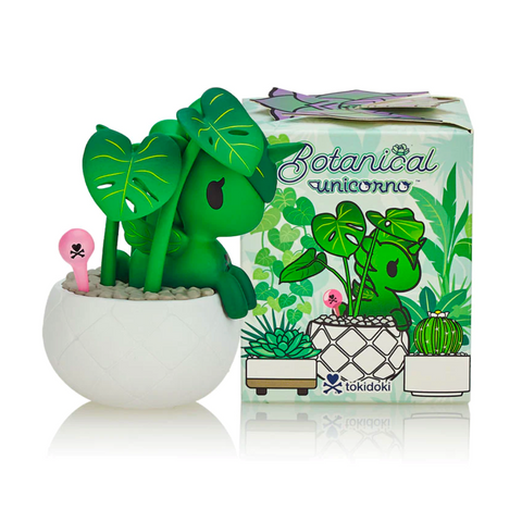 A small Tokidoki Botanical Unicorno - Blind Box figurine in a white planter with green leaves and a pink spade, accompanied by a decorated box featuring the same design from tokidoki (IT).