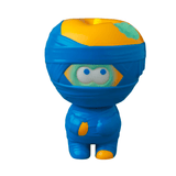 A small blue and yellow cartoon figure resembling a ninja, with a round head, large round eyes, and a teal leaf on its head. This adorable character is part of the Medicom (JP) VAG 36 - Yummy Mummy series, showcasing the charm of Japanese vinyl toys in gachapon figures.