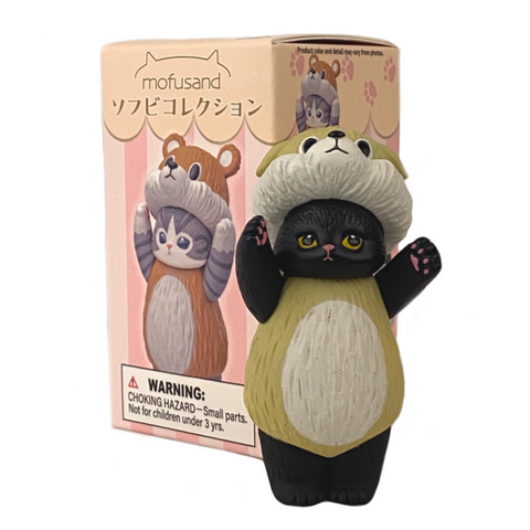 Here's your rewritten sentence:

The Mofusand Soft Vinyl Blind Box by Clever Idiots (US) contains a toy figurine of a Mofusand cat dressed in an adorable raccoon costume with its paws raised. The packaging features the same cute image and includes a visible warning label about choking hazards.