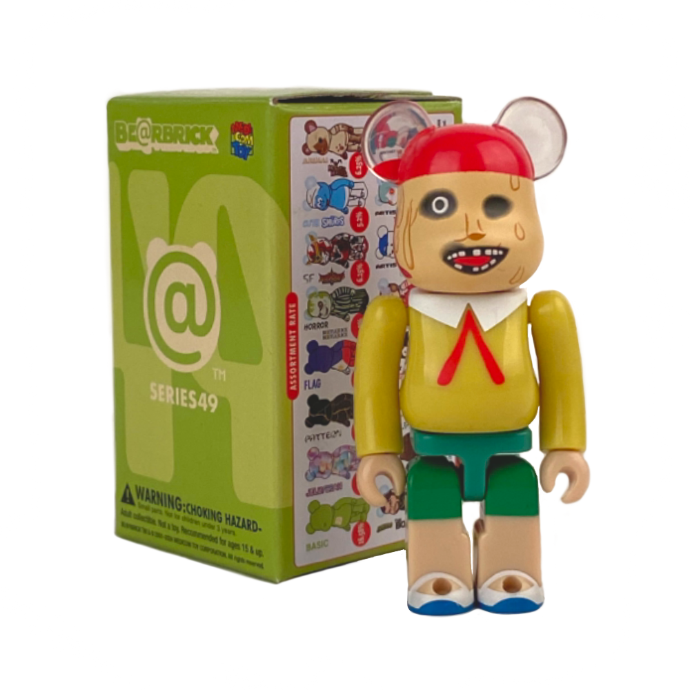 A Be@rbrick Series 49 figure with a cartoonish design is beside its green and white Medicom (JP) Be@rbrick Series 49 Blind Box, displaying various character illustrations.