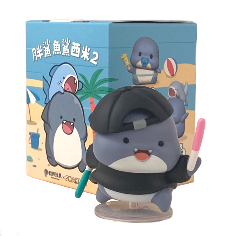 A charming blue shark figurine from Partner Toys' Shahimi Shark — Series 2 Blind Box collection holds pink and white sticks, set against a vividly illustrated beach-themed blind box.