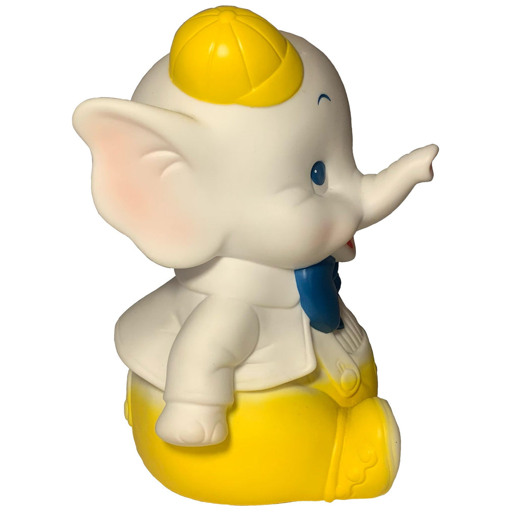 Side view of Yellow Bowtie Baby Elephant by Bitter Squeaks (US): a cartoon plush toy wearing a yellow cap, yellow pants, white shirt, bowtie, sitting and pointing forward.