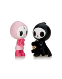 Two cute, anthropomorphic figurines are facing each other. The left one wears a pink hooded outfit, while the right one in black holds a small skull. This charming duo from the Tokidoki Adios & Ciao Ciao Together Forever Blind Box by tokidoki is cartoon-like with big eyes and simple features, embodying the essence of 'Til Death Do Us Part.