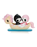 Two small, stylized cartoon characters, Adios & Ciao Ciao, in black and pink outfits ride in a whimsical, unicorn-themed boat with sprinkles on a blue base. This adorable scene is part of the Tokidoki Adios & Ciao Ciao Together Forever Blind Box series by tokidoki, capturing the essence of love and adventure.