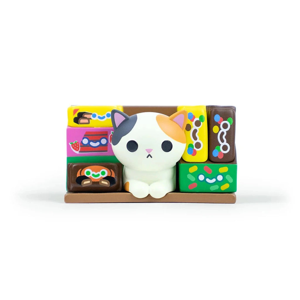 A small calico cat figurine from the 100% Soft Bodega Kitties — Series 1 Blind Box sits among colorful, patterned rectangular blocks on a brown base.