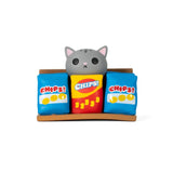 A gray cartoon cat figurine from the 100% Soft Bodega Kitties — Series 2 Blind Box peeks over three colorful chip bags on a small brown bodega shelf—perfect for any blind box collector.