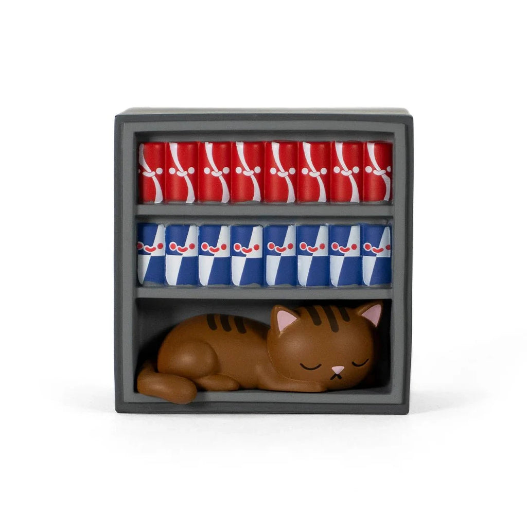 A Bodega Kitties — Series 2 Blind Box figurine by 100% Soft sleeps on a gray shelf beneath rows of red and blue soda cans.