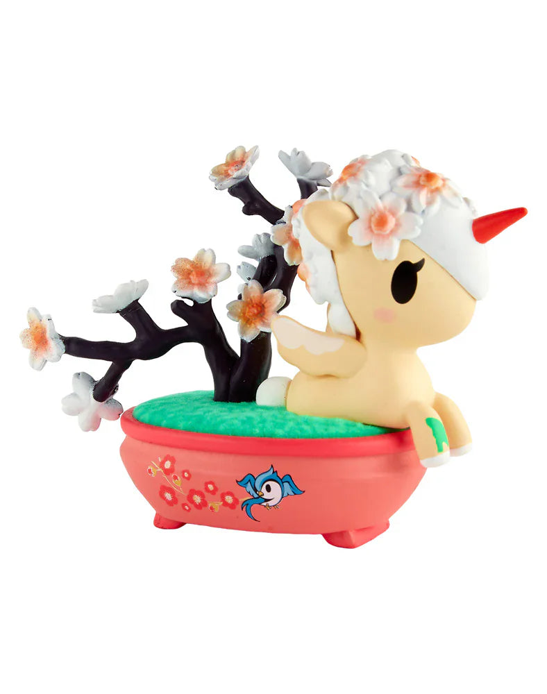 The tokidoki Botanical Bonsai Unicorno Blind Box features a charming figurine with a red horn in a pink bathtub, set among green grass and a black tree with pink flowers—ideal for miniature garden toy fans.