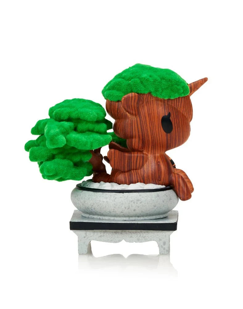 A Tokidoki Botanical Harmony Unicorno Blind Box figure by Tokidoki, styled as a tree trunk with green foliage in a bonsai pot on a small stand, is shown from the side against a white background.