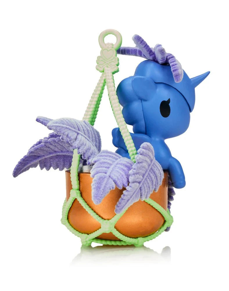 A Tokidoki Botanical Harmony Unicorno Blind Box figurine by Tokidoki sits in an orange hanging planter with purple leaves and a light green rope, combining collectible style with nature-inspired decor.