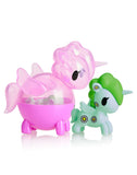 Two vibrant Unicorn figures, one with pink wings and the other green decorated with flower patterns, are showcased together. Experience the enchantment of these delightful figures from the Tokidoki Unicorno Capsule Cuties Blind Box collection.