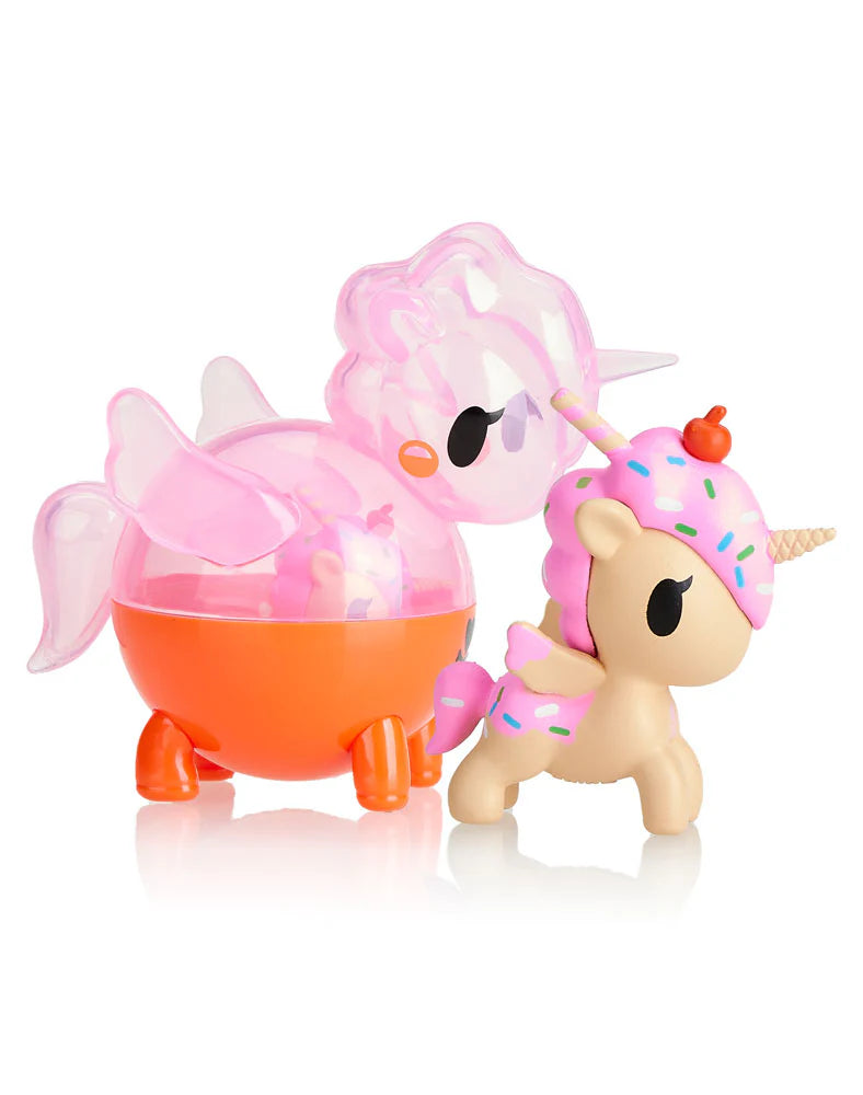 A Tokidoki Unicorno Capsule Cuties Blind Box reveals a pink transparent unicorn and a beige unicorn with a donut-themed mane, both standing side by side on a white background.