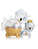 Two unicorn-themed figurines: one featuring a clear, dome-shaped design akin to a Tokidoki creation from the Unicorno Capsule Cuties Blind Box, positioned on a gleaming golden base; the other is silver with a golden crown and diamond details, standing beside it like an enchanting Tokidoki Capsule Cutie.