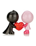 Two figurines facing each other, one black and one pink, holding a broken red heart. This 