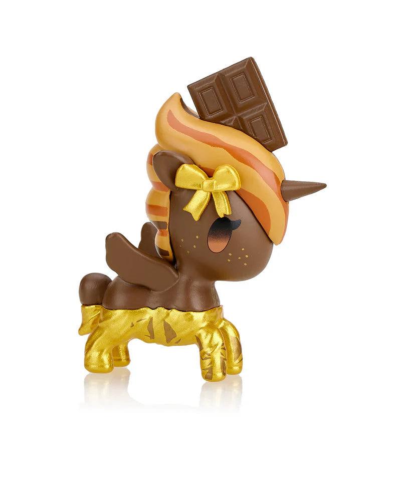 This small, squishy Unicorno figurine from Tokidoki showcases a charming chocolate-themed design. Adorned with a chocolate bar on its head, golden accents, and a cute bow, it's like unwrapping the magic of the Toki Mochi Donut Unicorno Blind Bag.