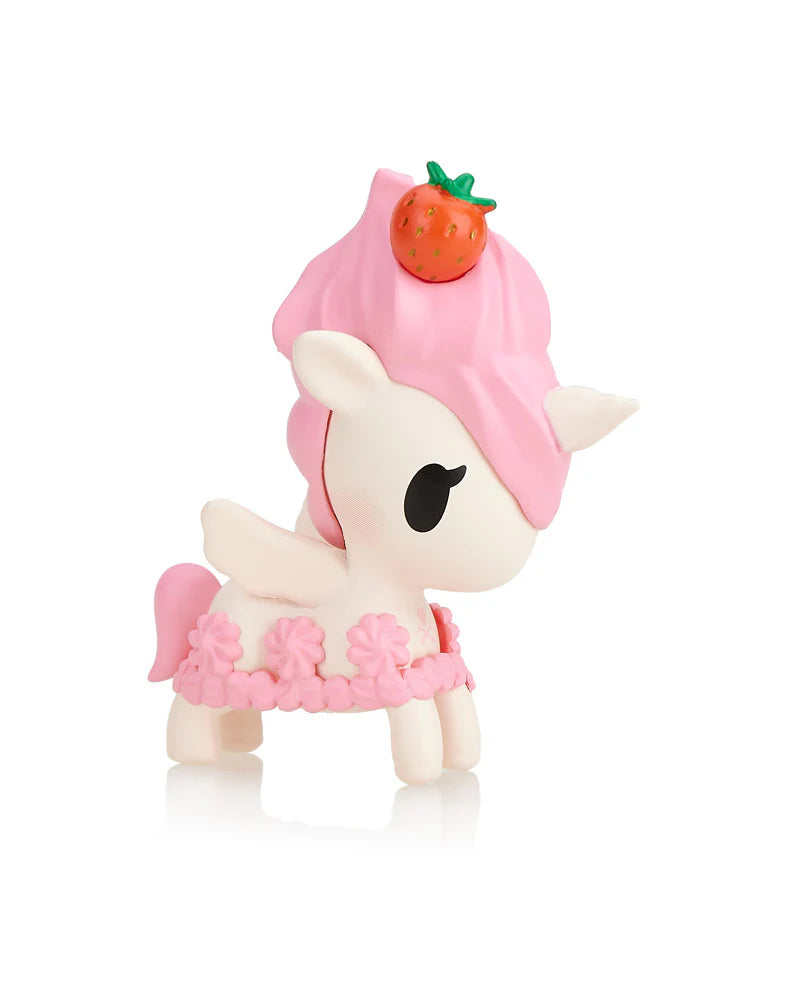 The Toki Mochi Donut Unicorno Blind Bag from Tokidoki captivates with its pink mane and tail, a strawberry sitting atop its head, and a delightful pink floral skirt. This charming figurine perfectly complements any Blind Box collection, embodying the essence of whimsical wonder.