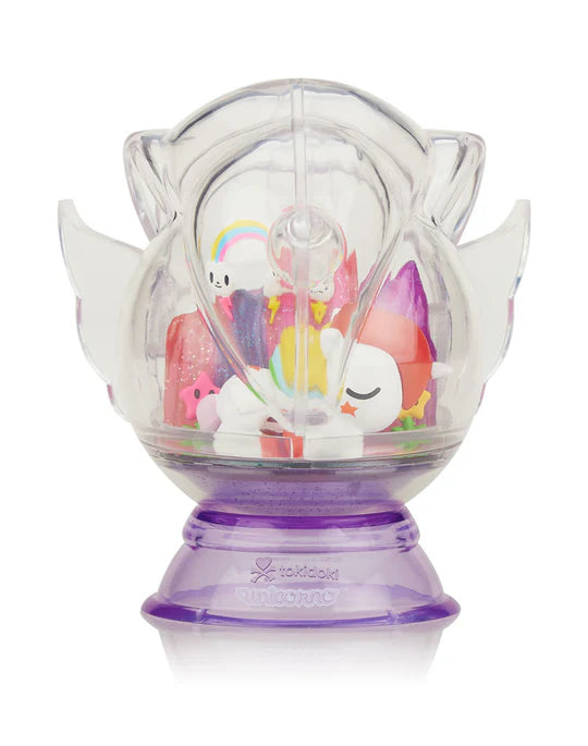 A toy with various small, colorful unicorn figures inside a clear, winged capsule sits on a purple base, ready to take you on a magical adventure. Discover the surprise inside each Tokidoki Dreaming Unicorno Blind Box by tokidoki.