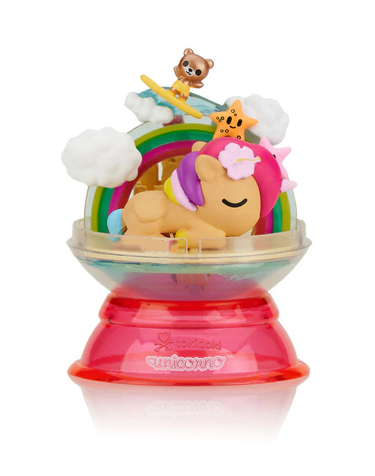 A colorful toy unicorn is dreaming under a rainbow with a surfing teddy bear and a star on top, all inside a clear dome with a pink base, as if embarking on a magical adventure from the Tokidoki Dreaming Unicorno Blind Box series by tokidoki.