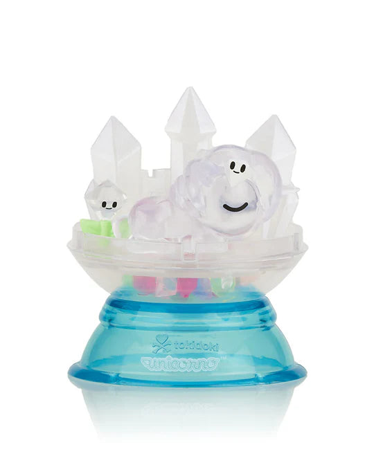 A small figurine of a smiling creature with clouds and crystal shapes, placed on a blue and transparent circular base with the word 