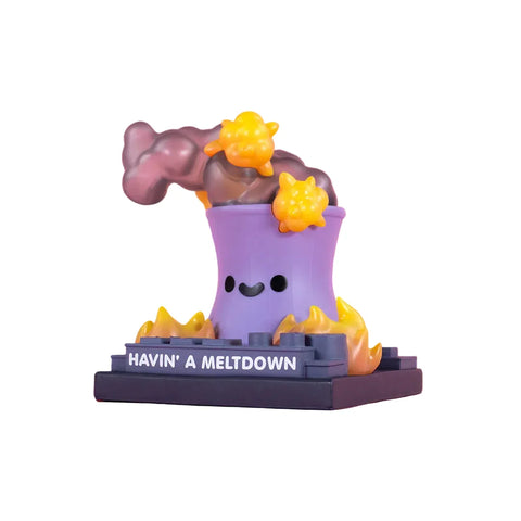 The 100% Soft Lil Meltdown Vinyl Figure is a cartoonish purple nuclear reactor cooling tower with a smiling face, surrounded by yellow flames and smoke, sitting on a base labeled "HAVIN' A MELTDOWN.