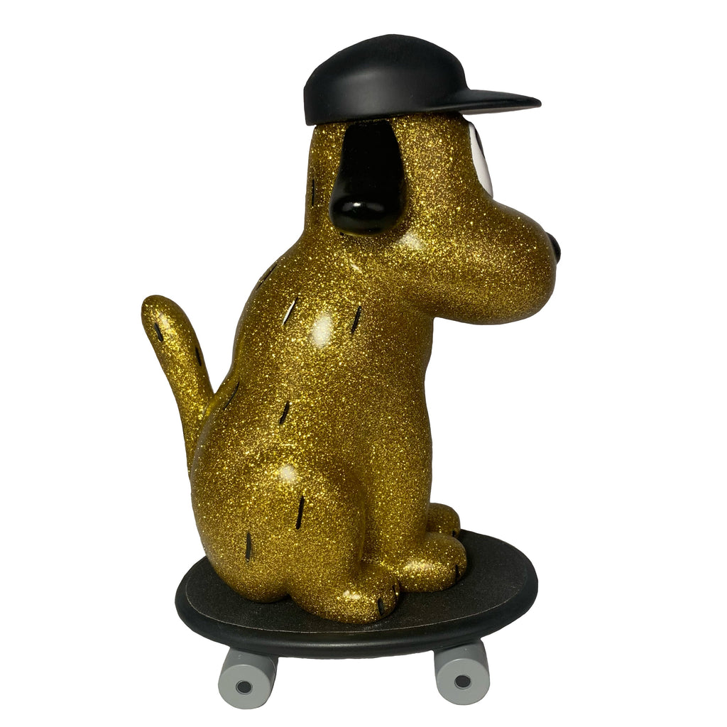 The How 2 Work One Chu Sk8- Gold features a gold glitter dog figure wearing a black cap, sitting on a black skateboard with gray wheels, facing right.