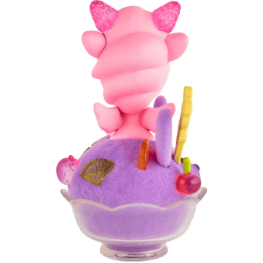 A special edition Shaved Ice Dreams Unicorno Honey Bunny figure by tokidoki, featuring pink, cartoonish horns, sits in a glass bowl of purple shaved ice dessert topped with colorful decorations, viewed from behind.