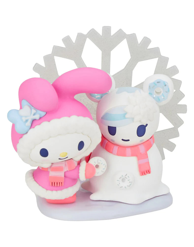 Two adorable figures dressed in winter clothing stand side by side; one is designed to look like a pink snowman, while the other resembles a white bear. A snowflake background enhances the winter theme, capturing the charm of the tokidoki x Hello Kitty and Friends Winter Dreams Blind Box by Tokidoki.