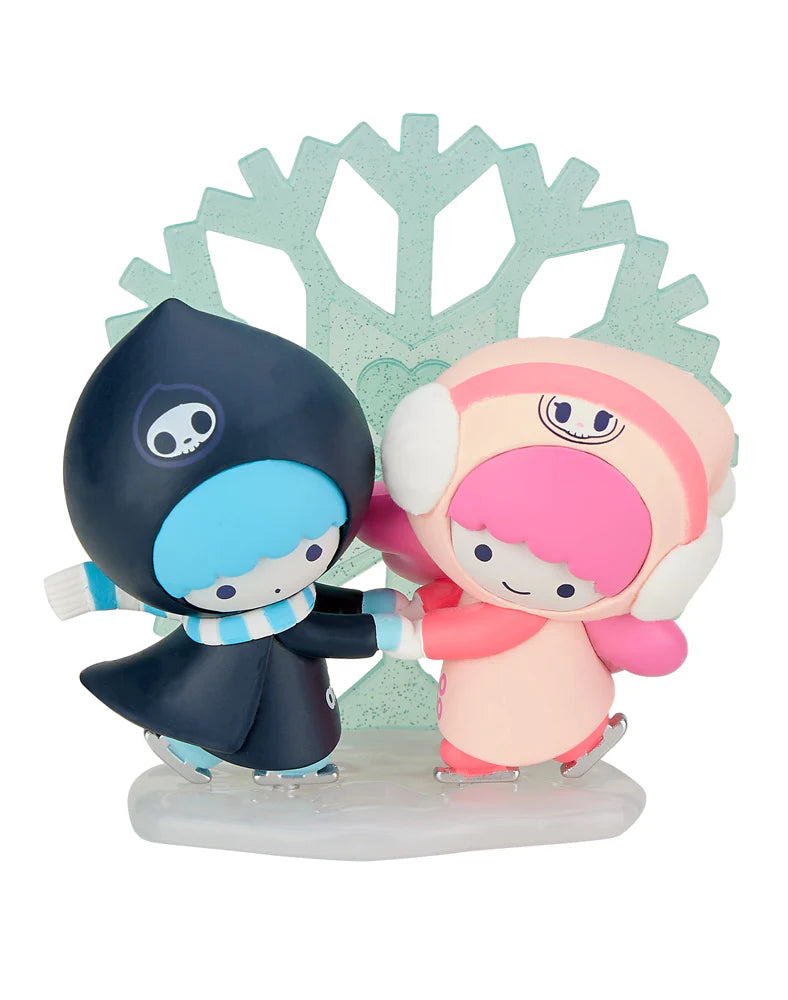 Two charming figurines from the tokidoki x Hello Kitty and Friends Winter Dreams Blind Box gracefully ice skate against a green snowflake backdrop. One wears a stylish black outfit while the other shines in pink, perfectly embodying the playful spirit of Tokidoki's collection.