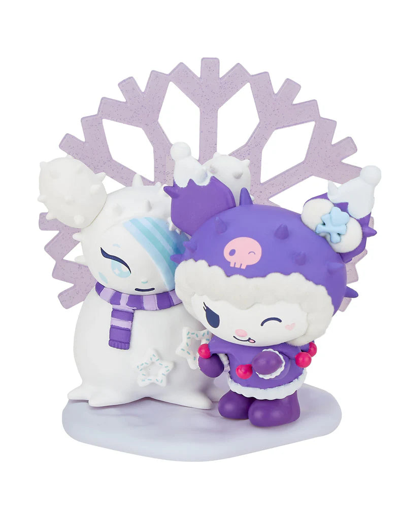 Two figurines dressed in purple, adorned with snow-themed accessories, stand before a large snowflake decoration, perfectly capturing the enchanting spirit of the Tokidoki x Hello Kitty and Friends Winter Dreams Blind Box.