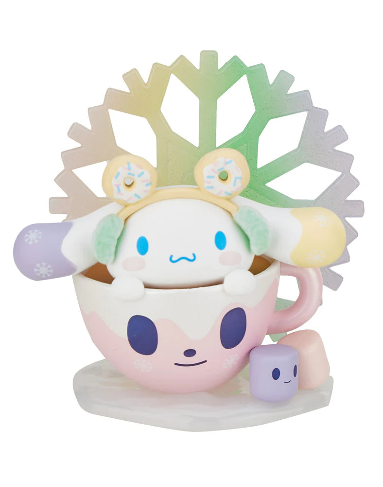 A charming character adorned with colorful earmuffs is nestled in a pink teacup featuring a smiling face, accompanied by a small cube-like figure and set against a vibrant snowflake backdrop. This scene brings to life the enchanting spirit of the Tokidoki x Hello Kitty and Friends Winter Dreams - Cinnamoroll (Special Edition) by Tokidoki.