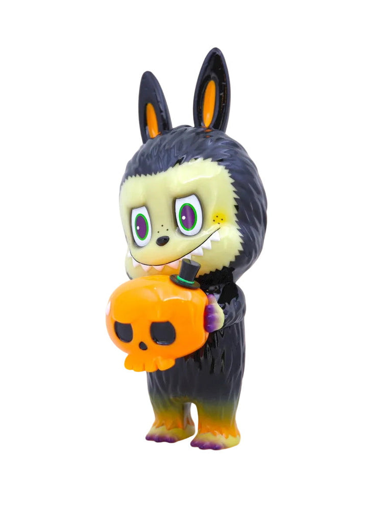 The Labubu - Halloween by How2Work (HK) is a small figurine of a black-furred, cartoonish creature with rabbit ears and fangs, holding an orange pumpkin-shaped skull—a unique collectible toy.