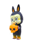 The Labubu - Halloween by How2Work (HK) is a small figurine of a black-furred, cartoonish creature with rabbit ears and fangs, holding an orange pumpkin-shaped skull—a unique collectible toy.