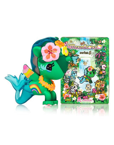 A green Tokidoki Mermicorno Series 8 Blind Box with a flower on it sits next to a book.