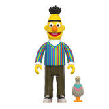 A plastic figurine of a character wearing a colorful striped shirt stands next to a smaller figurine of a gray bird with a colorful vest, both part of the 3.75” scale ReAction Figures from the Sesame Street Series 1 Super 7 Blind Box collection by Super 7 (US).