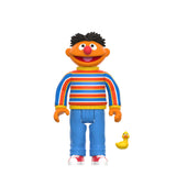 A cartoon character with orange skin, a red nose, and black hair stands smiling in a striped sweater and blue pants next to a small yellow rubber duck, looking like they just stepped out of the Sesame Street Series 1 Super 7 Blind Box collectible toy set by Super 7 (US).