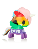 A Unicorno Prisma wearing a rainbow hat is sitting on top of a white background. (Brand Name: tokidoki)