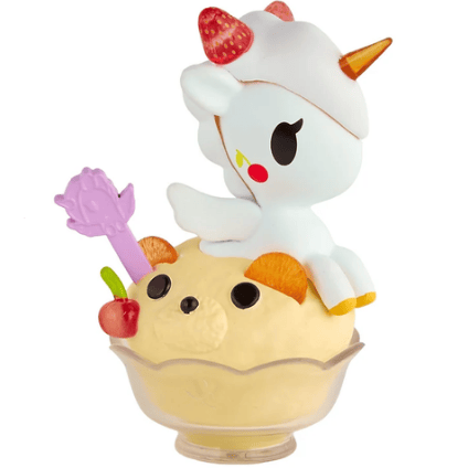A charming figurine from the Shaved Ice Dreams Unicorno Blind Box by tokidoki features a unicorn perched on a scoop of ice cream adorned with bear ears, a cherry, and a purple hand-shaped pick, all served in a glass dessert bowl.