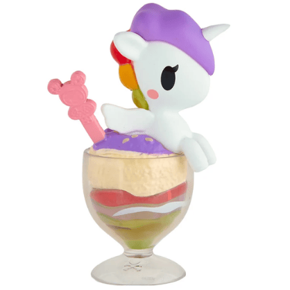 The Shaved Ice Dreams Unicorno Blind Box by tokidoki features a collectible figurine sporting a purple hat, perched on top of a layered parfait in a glass cup with vibrant colors and finished with a pink bear-shaped stick—an ideal surprise for fans of blind box collectibles and unique tokidoki toys.
