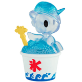 A translucent blue unicorn from the tokidoki Shaved Ice Dreams Unicorno Blind Box perches on a mound of blue ice in a white cup decorated with blue waves and a red Japanese kanji. This striking collectible also features a tiny yellow figure peeking out from the ice—an exciting surprise for fans who love discovering hidden treasures in every blind box.