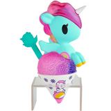 A turquoise unicorn toy with a pink mane and white horn from the tokidoki Shaved Ice Dreams Unicorno Blind Box sits atop a colorful snow cone in a decorated paper cup with a green spoon, all displayed on a small clear stand—making it the perfect collectible surprise!.