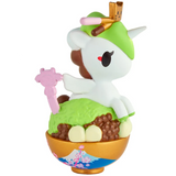 The tokidoki Shaved Ice Dreams Unicorno Blind Box features an adorable Unicorno figurine sporting a green hat, nestled in a bowl adorned with floral and fan designs and filled with colorful treats like brown and yellow balls—an ideal collectible for fans of blind box surprises.